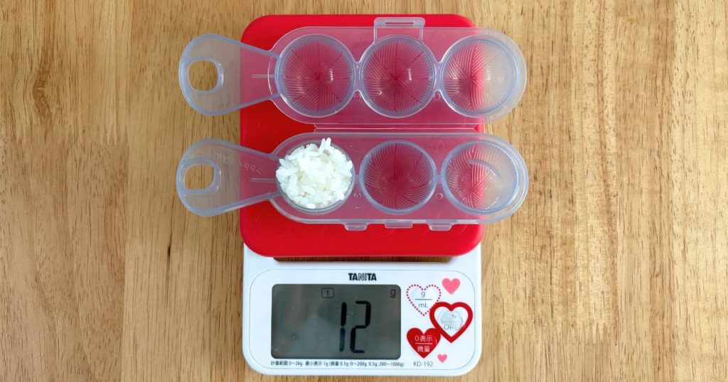 ダイソーの「まんまるおにぎりメーカー」にご飯を詰めて、おにぎり1個あたりの重さを計量している写真